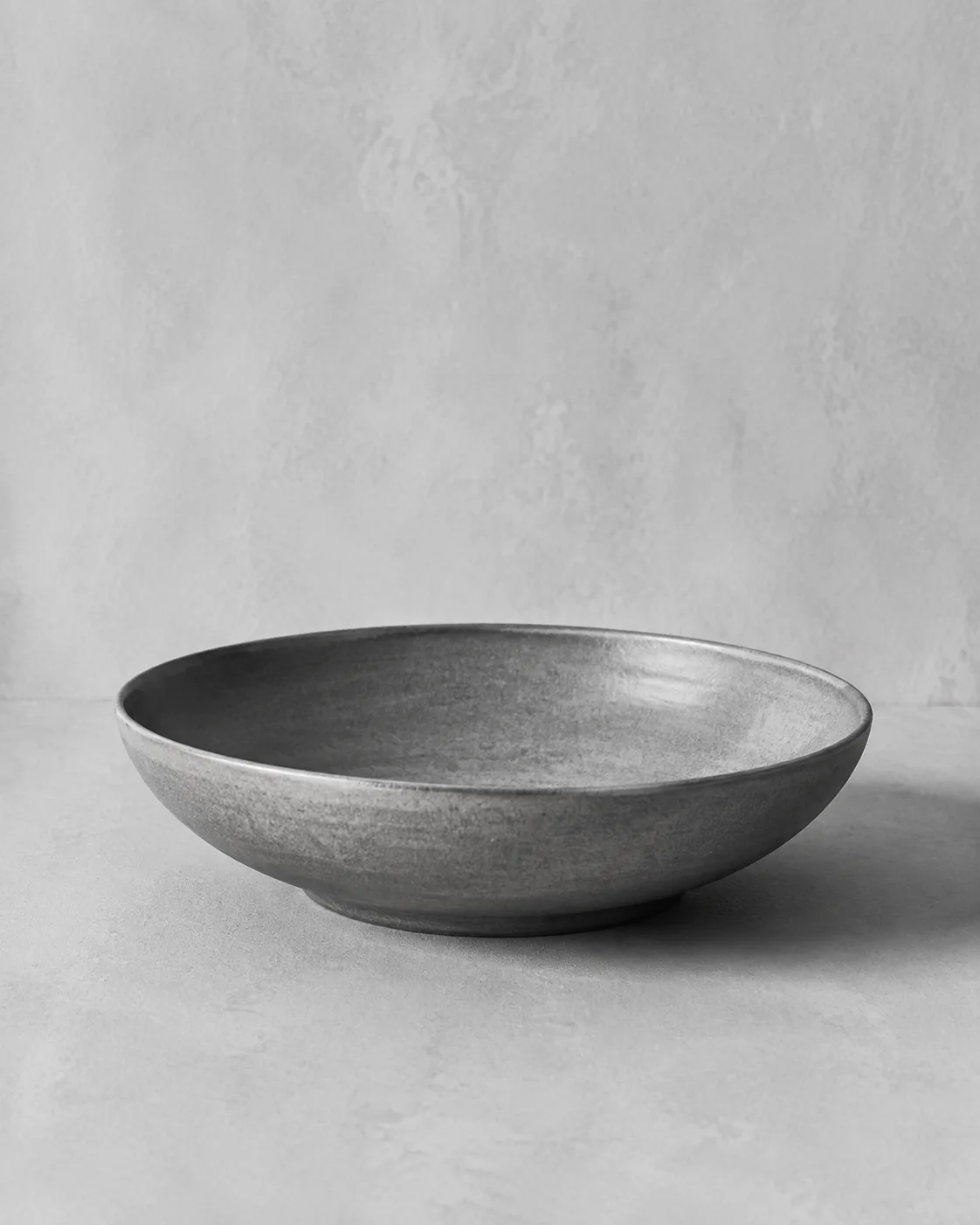 Illustrative monochrome image: Low profile hand-thrown ceramic serving bowl with natural warm glaze