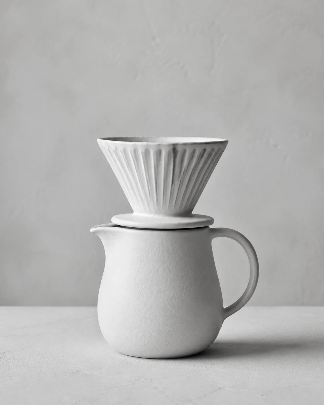 Illustrative monochrome image: Ceramic coffee pour over dripper and matching carafe on wood counter