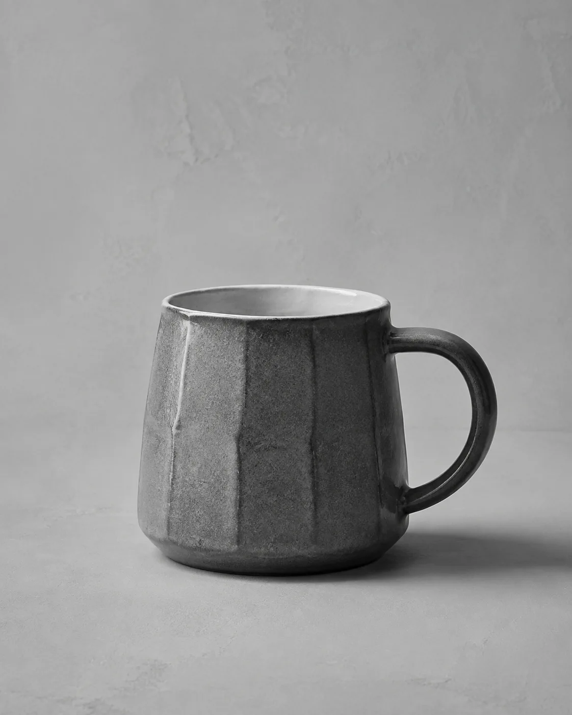 Illustrative monochrome image: Handmade ceramic mug with celadon glaze and pulled handle