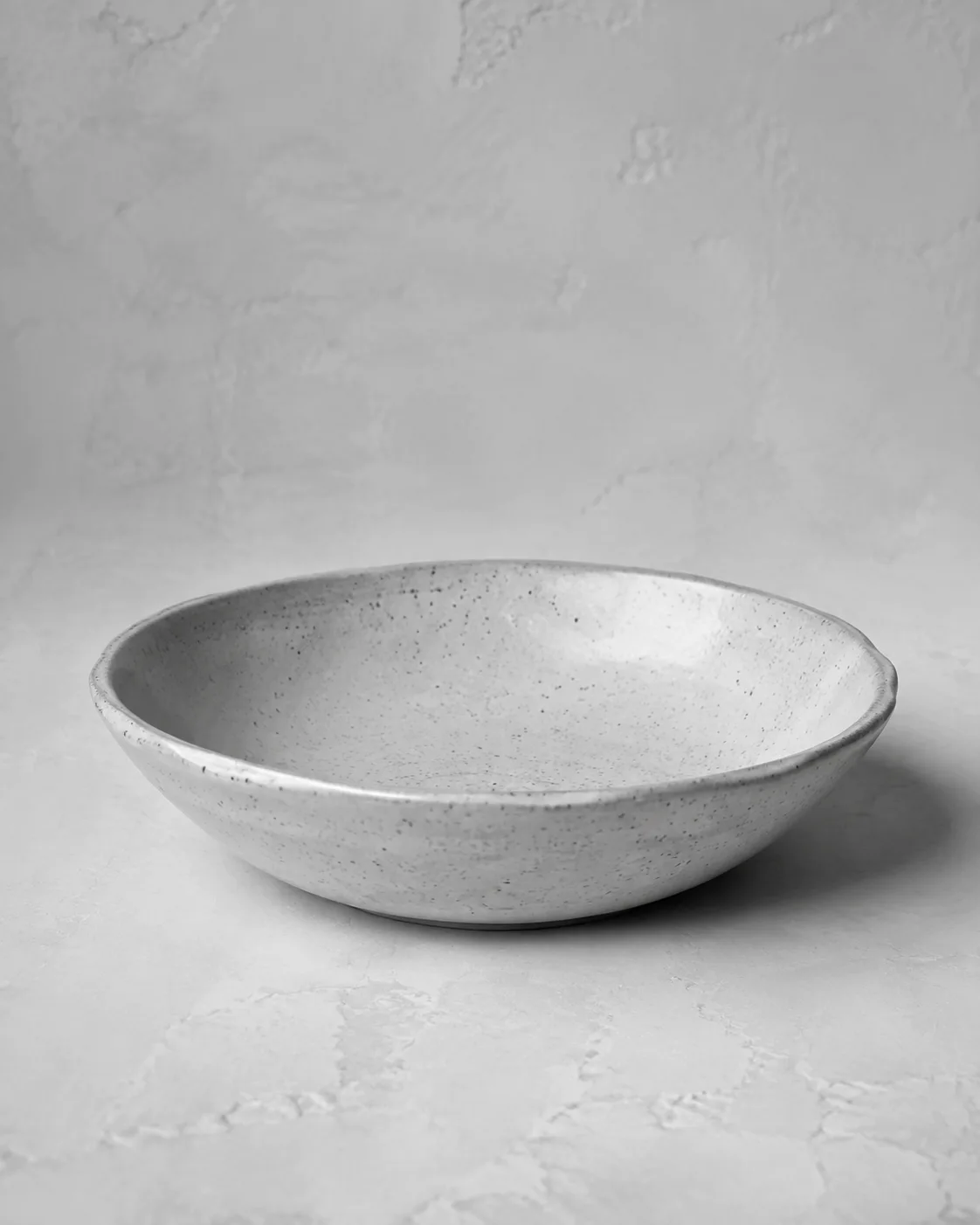 Illustrative monochrome image: Shallow handmade ceramic pasta bowl with gentle organic rim