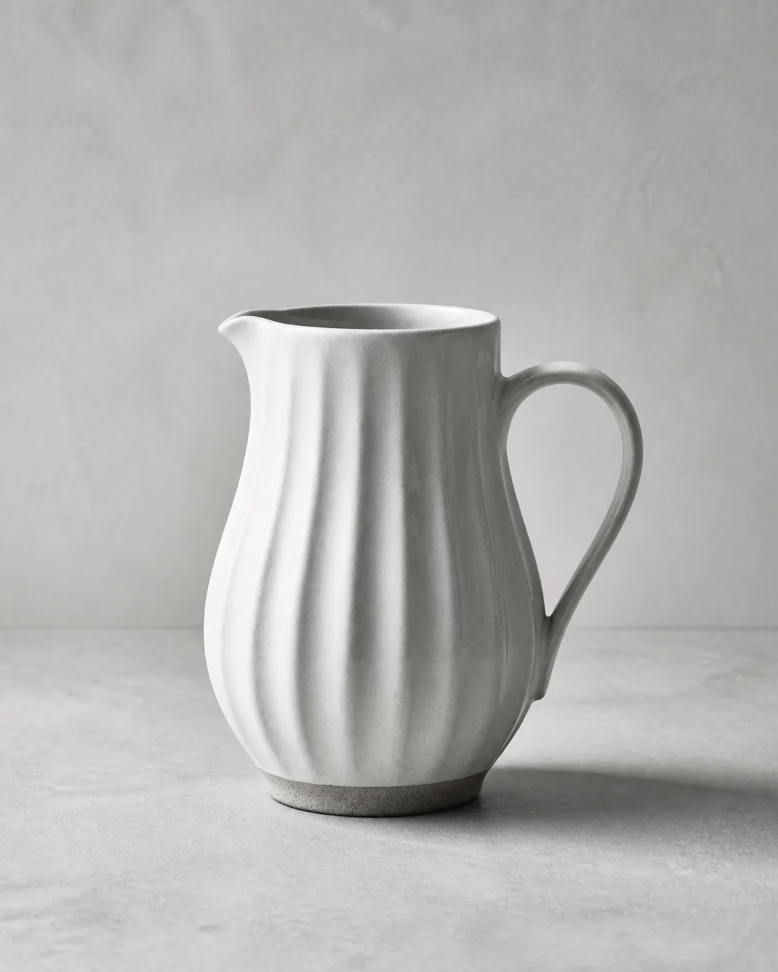 Illustrative monochrome image: Handmade fluted stoneware pitcher with matte white glaze